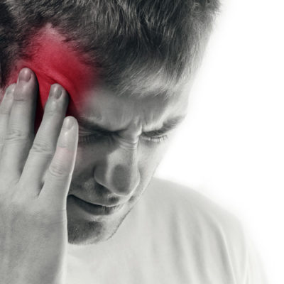 black and white image of man holding hand to this head which is colored red to show that he is suffering from migraine pain
